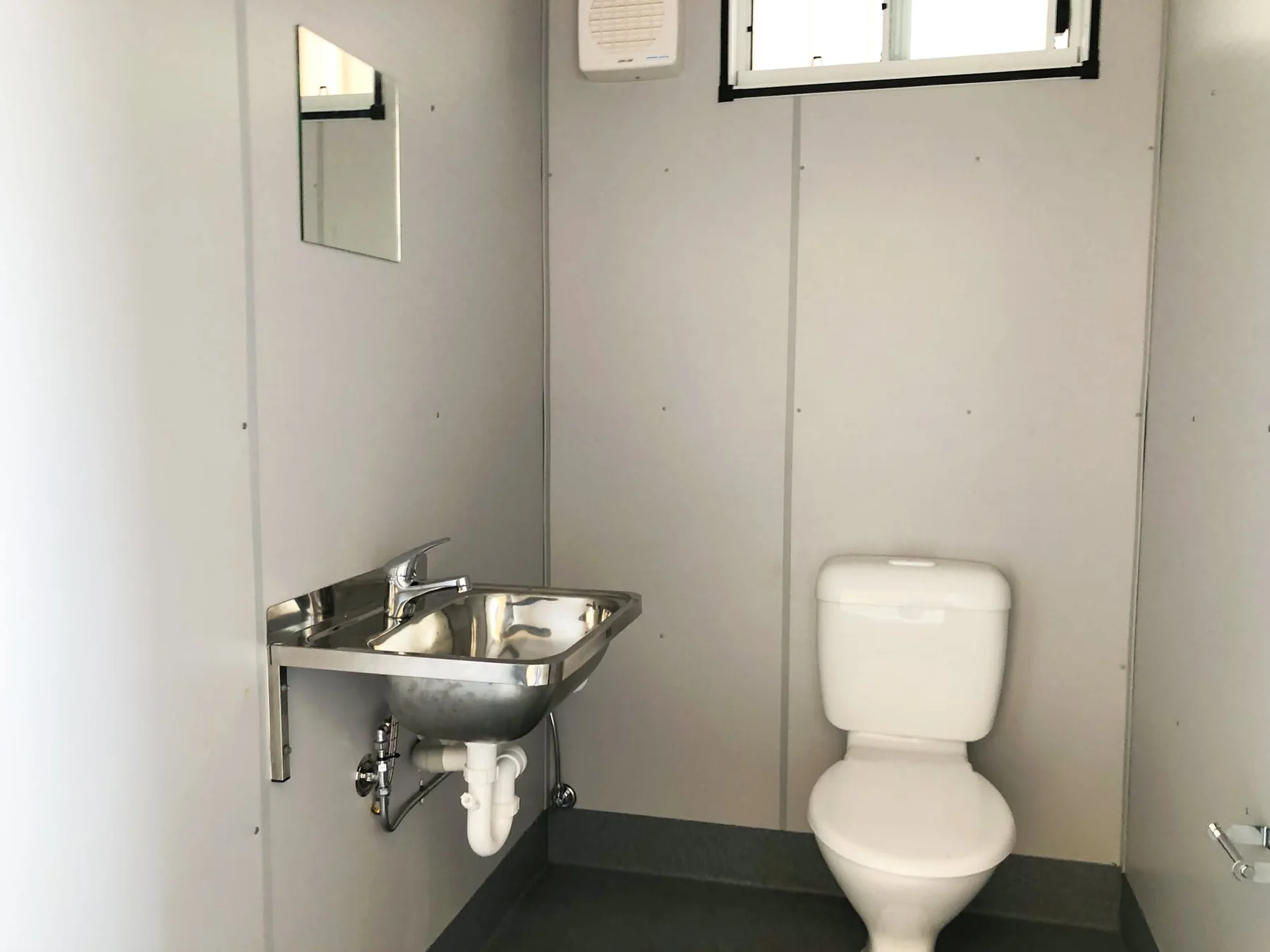 Toilet compartment with a toilet pan, stainless steel hand basin, mirror and high window