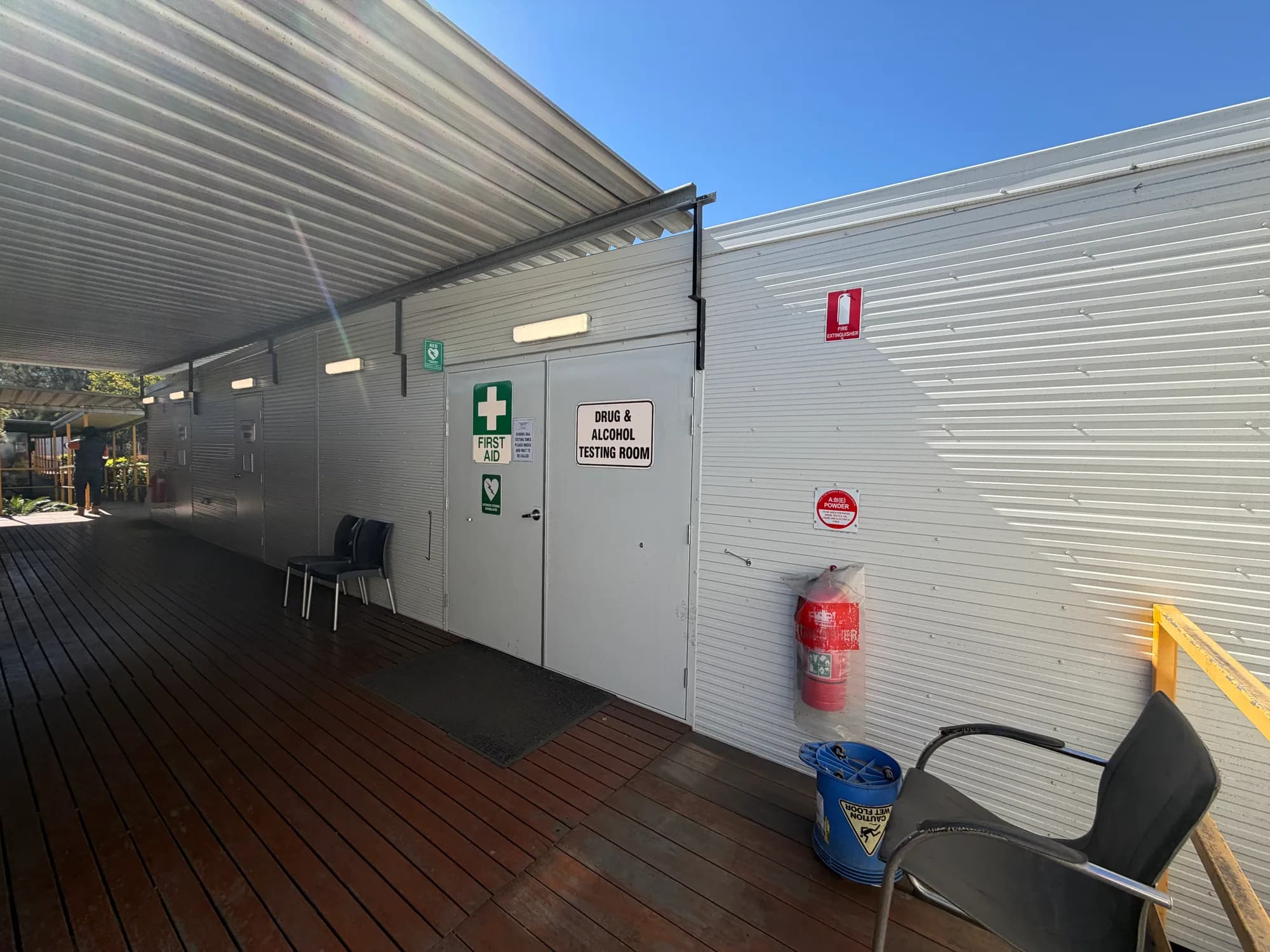 First-aid building entrance opening onto a covered timber deck beside other site buildings