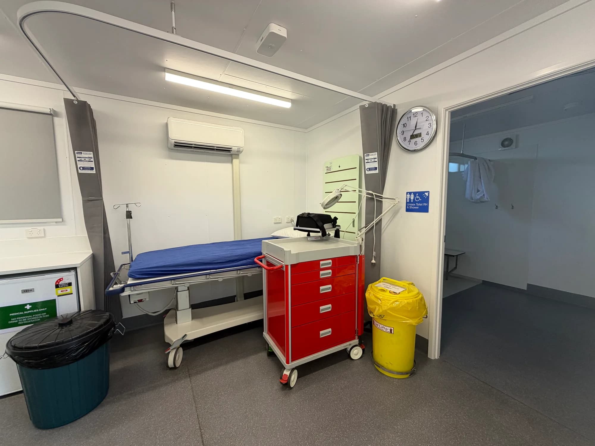 Treatment bed beneath a curtain track, with a trolley and a doorway to an amenities room