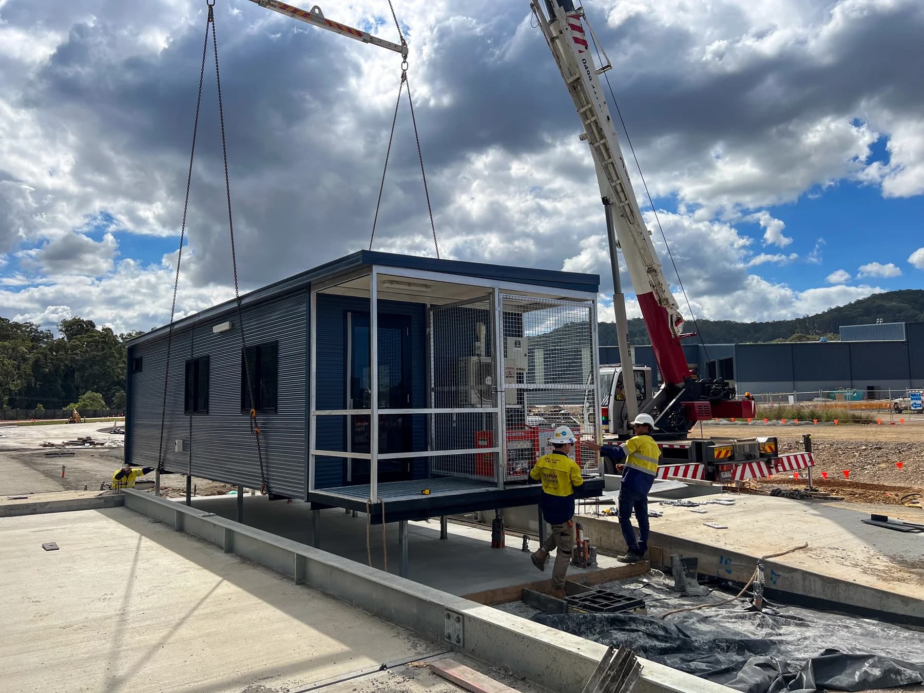 Dark-clad gatehouse with a screened end platform during crane placement onto steel posts
