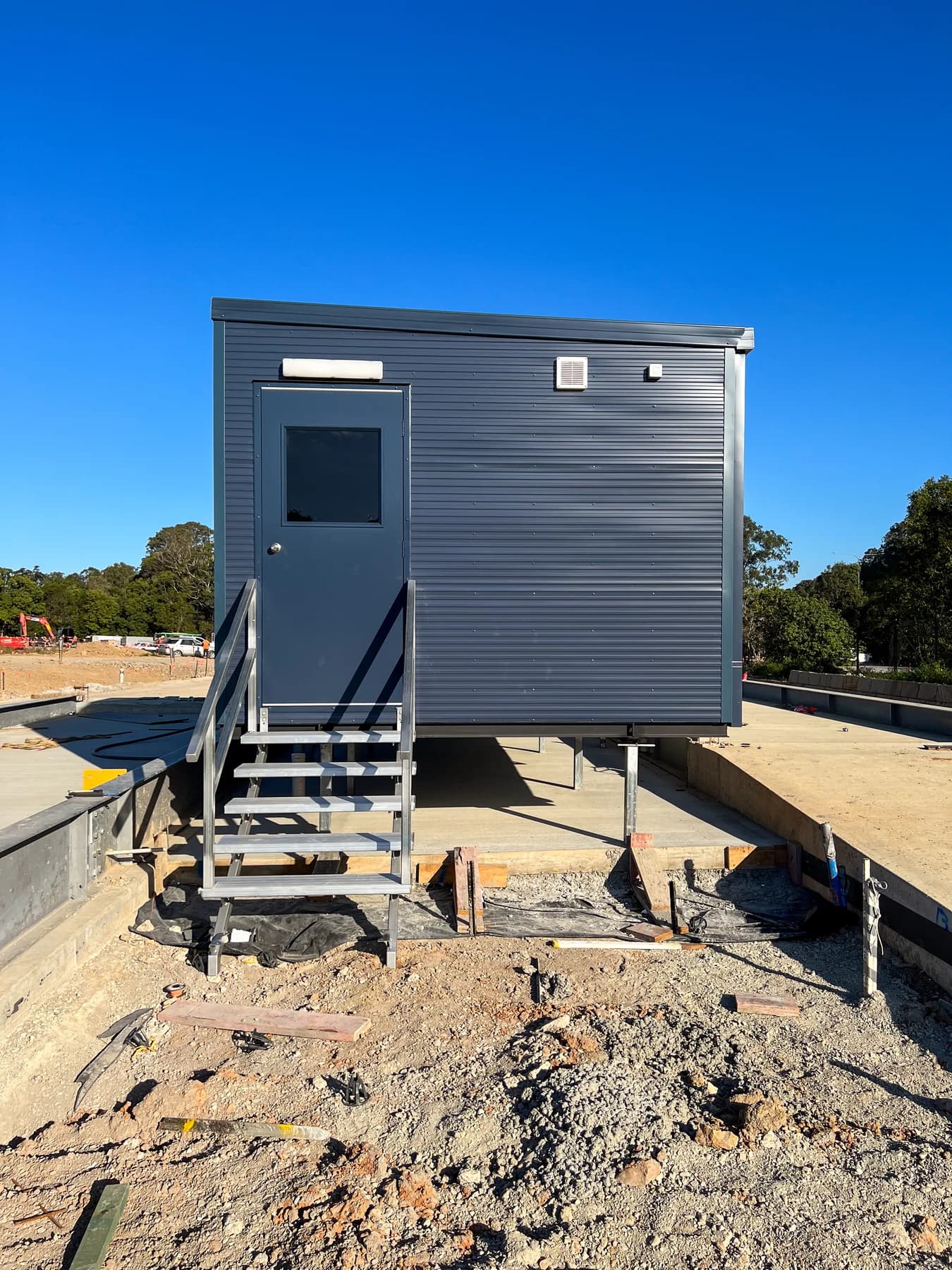 Installed gatehouse on steel supports with stairs and handrails beside ongoing ground works