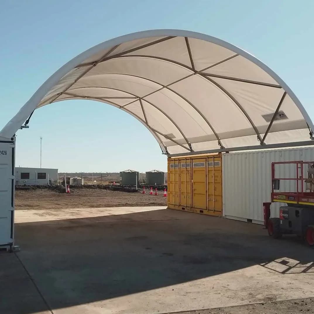 Arched fabric shelter spanning between containers above a concrete area