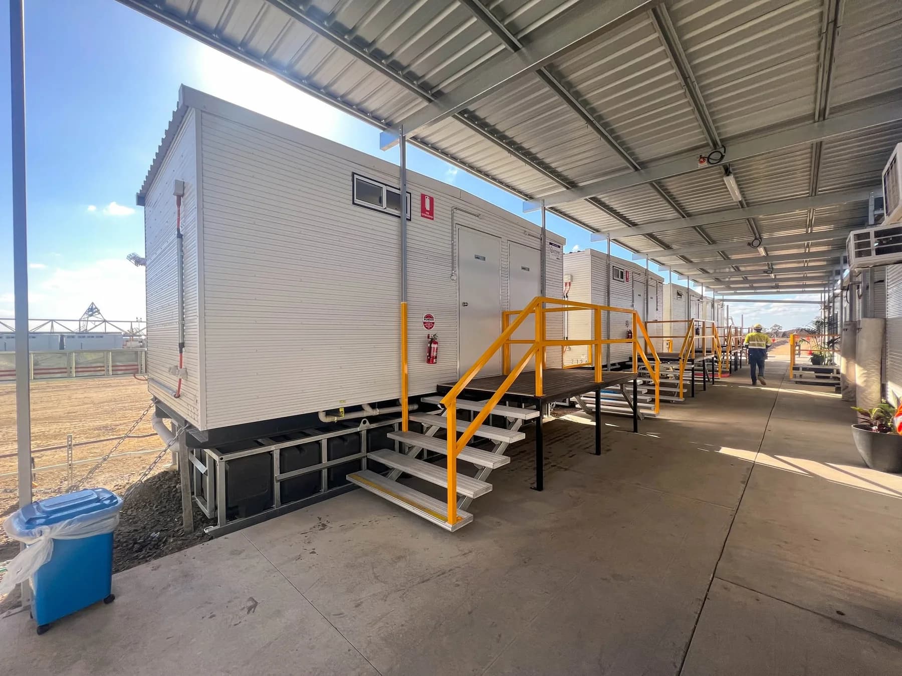 Covered concrete walkway between modular buildings with yellow-railed stairs and visible building tie-down chains