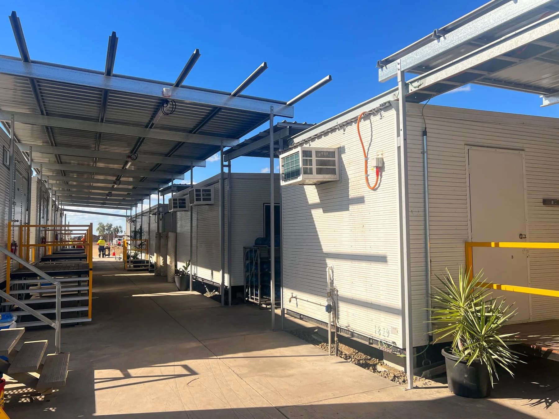 Concrete walkway between modular buildings with partially roofed steel framing overhead