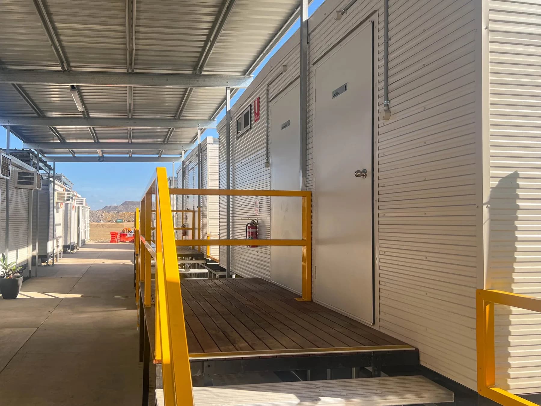 Close view of timber landing, yellow handrails and metal stair treads beside a modular building