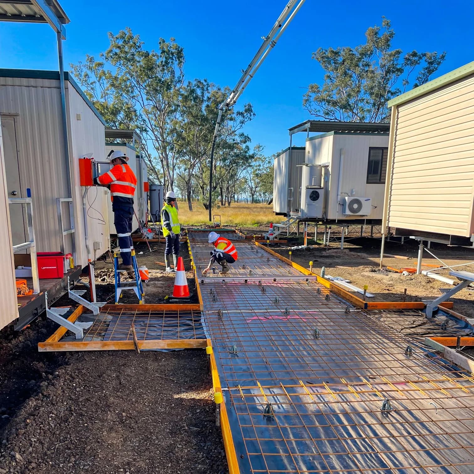 Crew placing reinforcing mesh and formwork for a concrete path between rows of site buildings