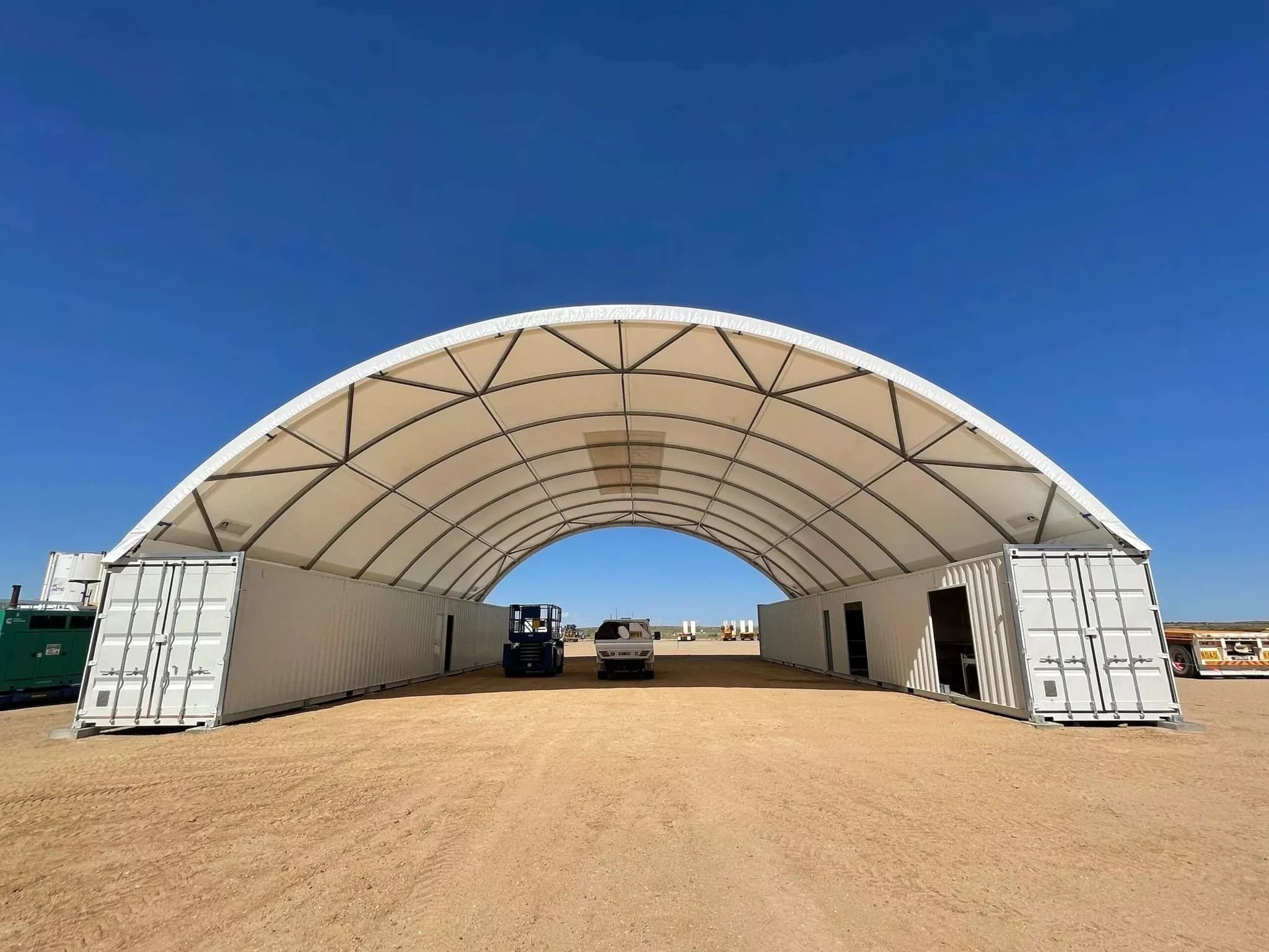 Arched fabric shelter spanning two rows of shipping containers on a gravel pad