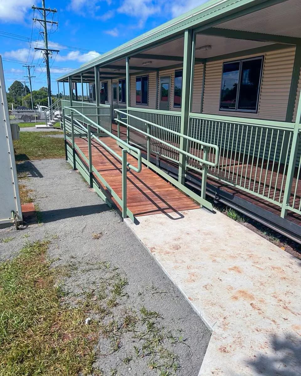 Timber access ramp with green handrails leading from a concrete path to the school veranda