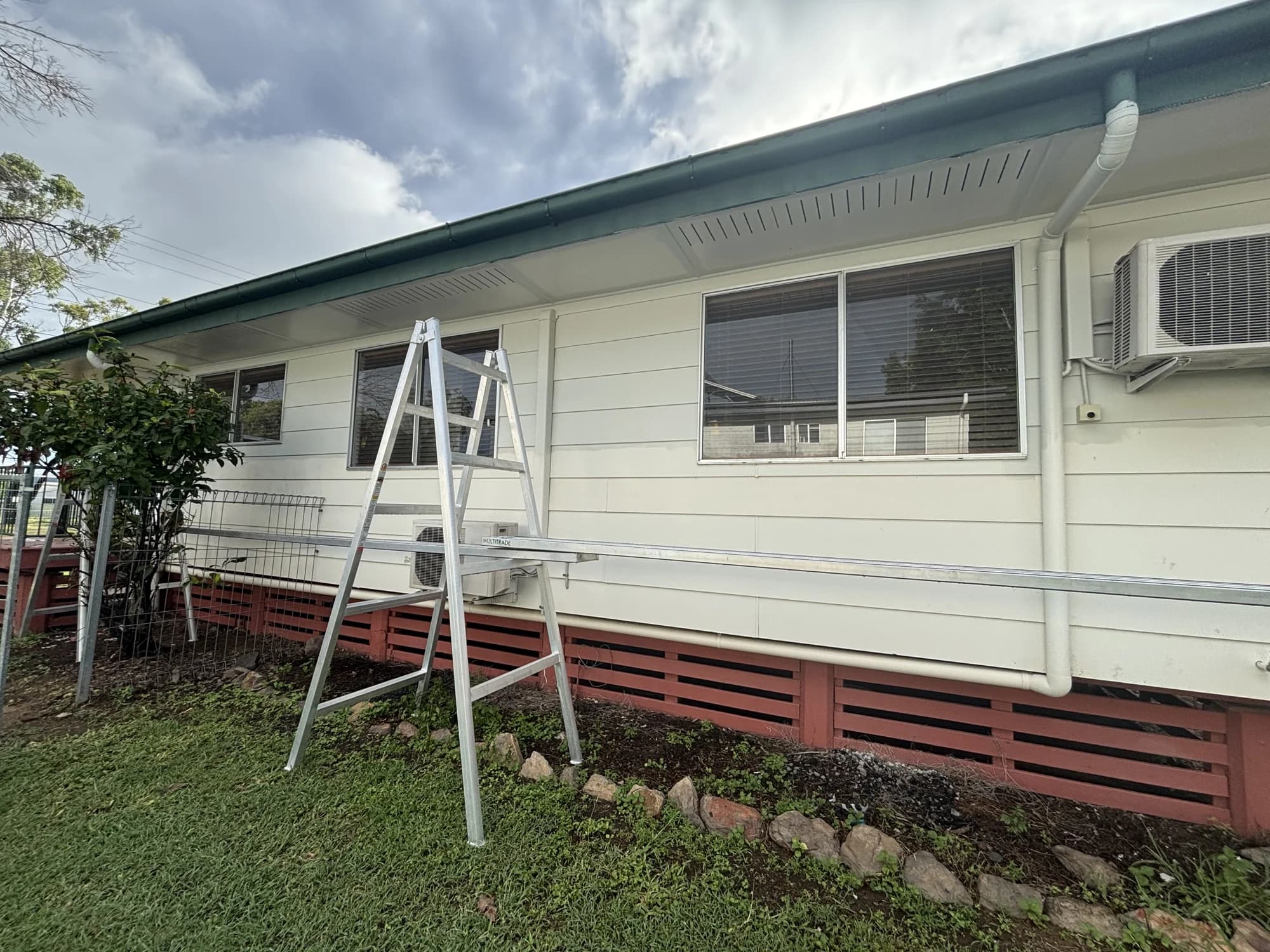 Residential home exterior during exterior maintenance, with access trestles and a plank beside the wall
