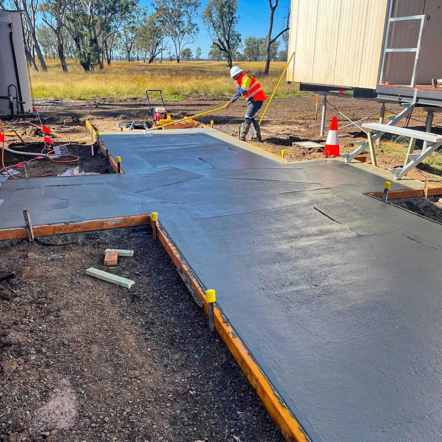 Worker finishing wet concrete at a path junction beside partially assembled stairs