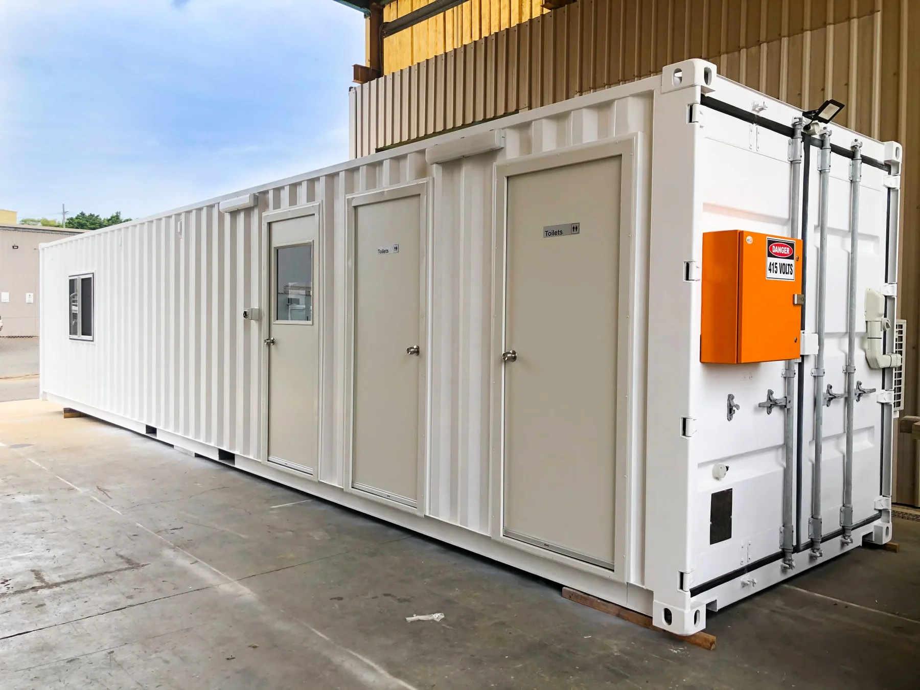 White converted shipping container with a crib-room entrance, two toilet doors and an external orange distribution board