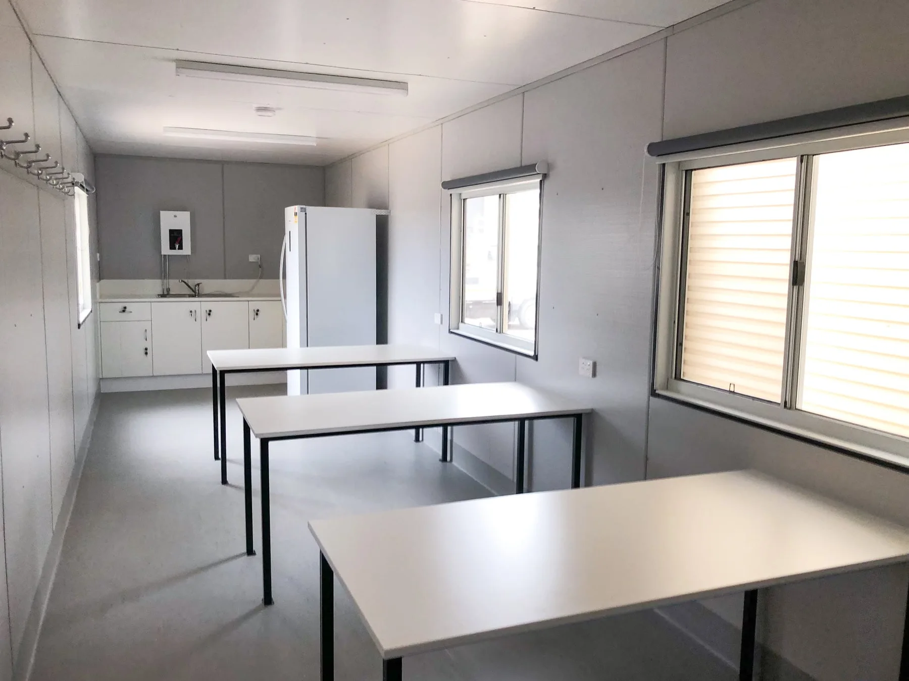 Container interior with tables, windows, wall hooks, kitchenette cabinets, sink and refrigerator