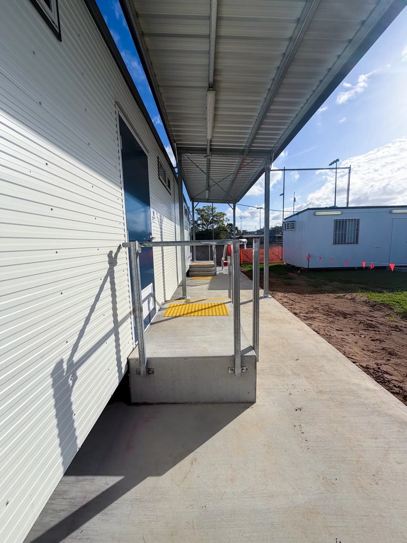 View along the covered concrete access walkway with entry landings, handrails and tactile indicators