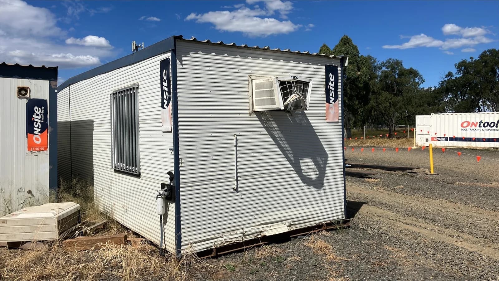 Original portable building exterior with weathered cladding, a barred window and an air-conditioning opening
