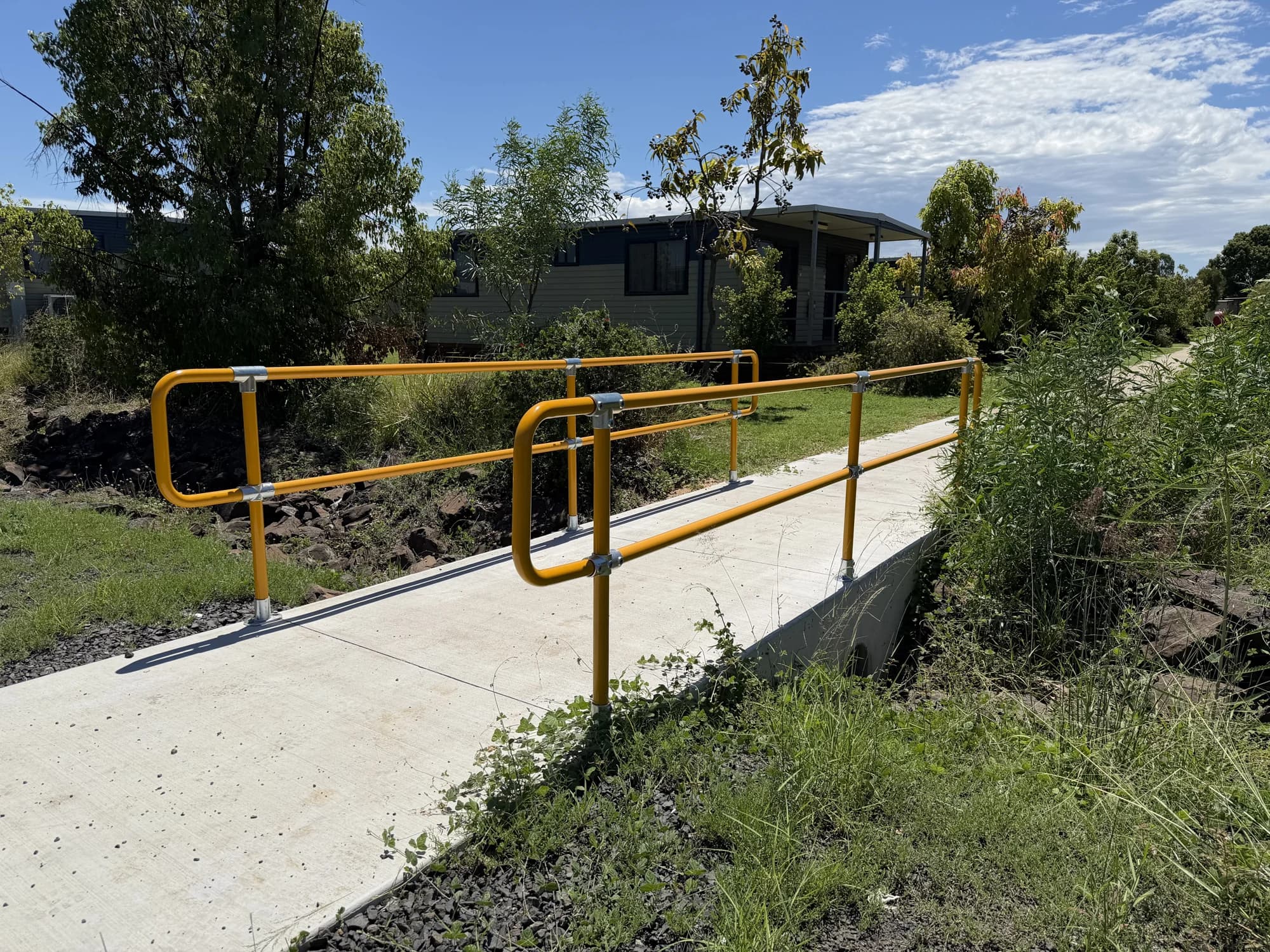Yellow handrails on both sides of a concrete pathway crossing