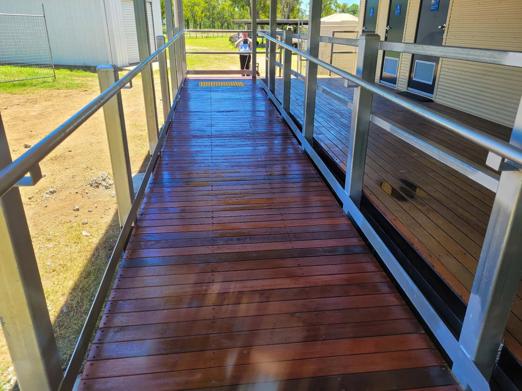 Timber access ramp with continuous metal handrails and a yellow tactile surface