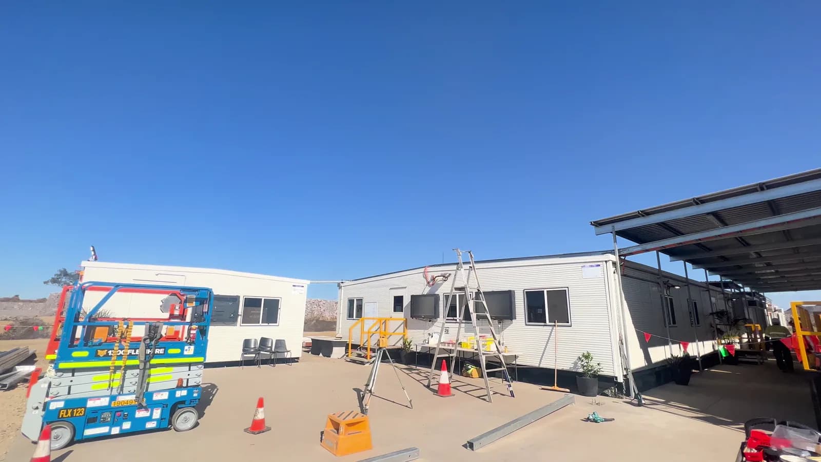 Modular buildings and awning with a scissor lift, ladders and construction materials on the concrete area